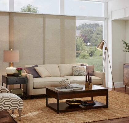 Cozy living room with beige sofa and large windows overlooking a green garden.
