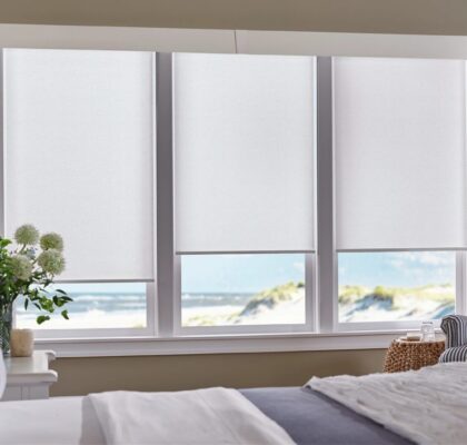 Window with white blinds overlooking a beach and ocean.