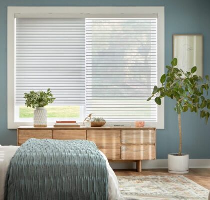 Cozy bedroom with wooden furniture, white blinds, and green plants.